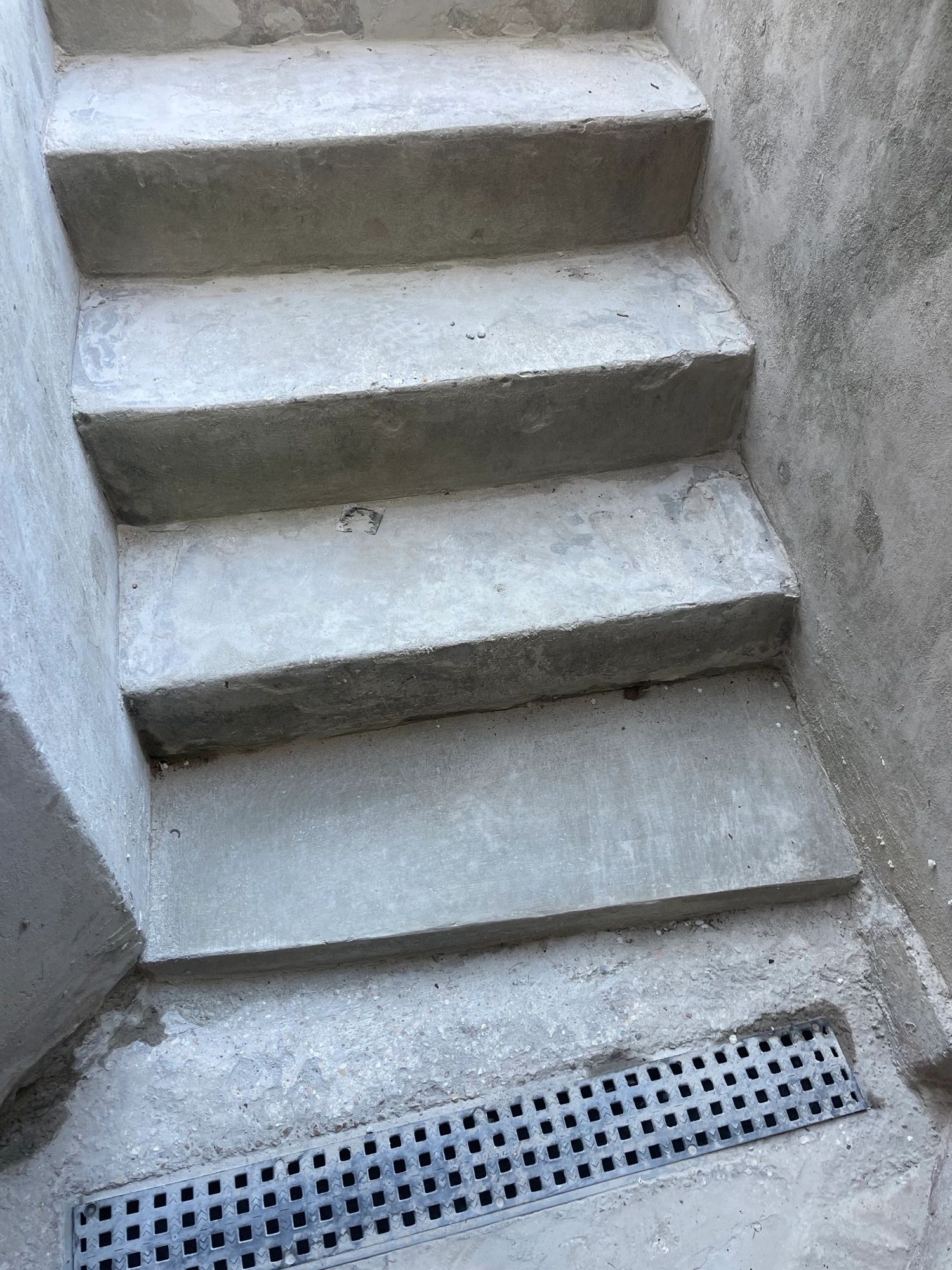 Repaired concrete stairway with smooth restored steps and drainage grate after concrete restoration