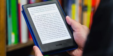 A hand holding an eBook reader, while standing in a library