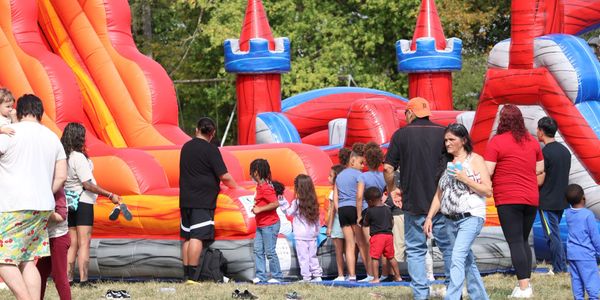 Children and adults gather around an inflatable slide at a park event.