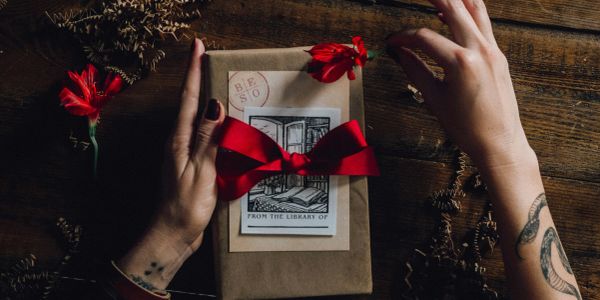 Hands holding a wrapped gift with a red bow and flowers.