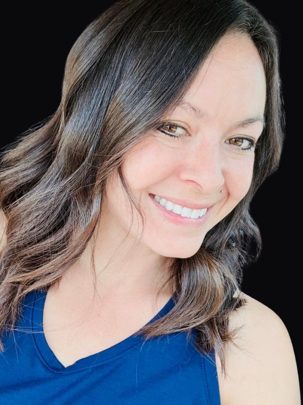 Woman with brown hair smiling against black background.