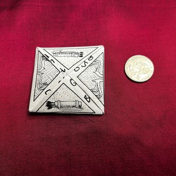 Decorative square pendant with coin for scale on red fabric.