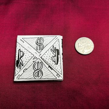 Hand-drawn symbols on a small square paper next to a coin.