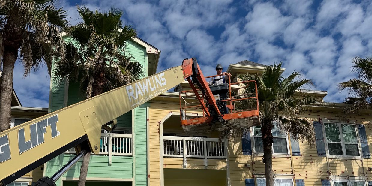 Worker using lift for building maintenance on colorful apartment complex.