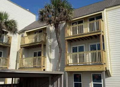 Wooden balconies on a beige apartment building with palm trees.
