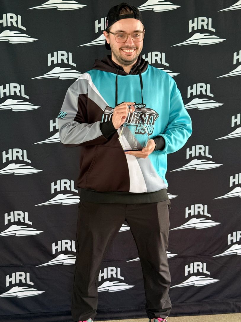 Man holding a clear trophy, smiling in front of an HRL backdrop.