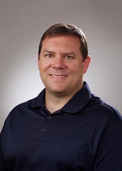 Man in a navy polo shirt smiling.
