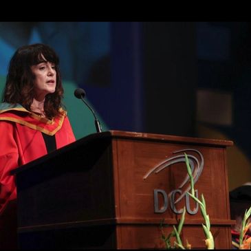Prof Maura McAdam in a red gown reading   a citation at a DCU lectern