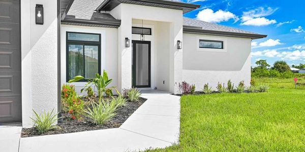 Modern white house entrance with a neatly landscaped front yard and bright blue sky.
