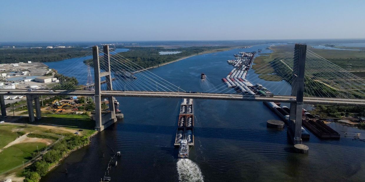 A large barge with containers passing under a cable-stayed bridge.
