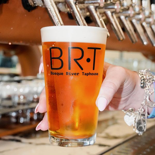 Hand holding a pint of beer at Bosque River Taphouse.