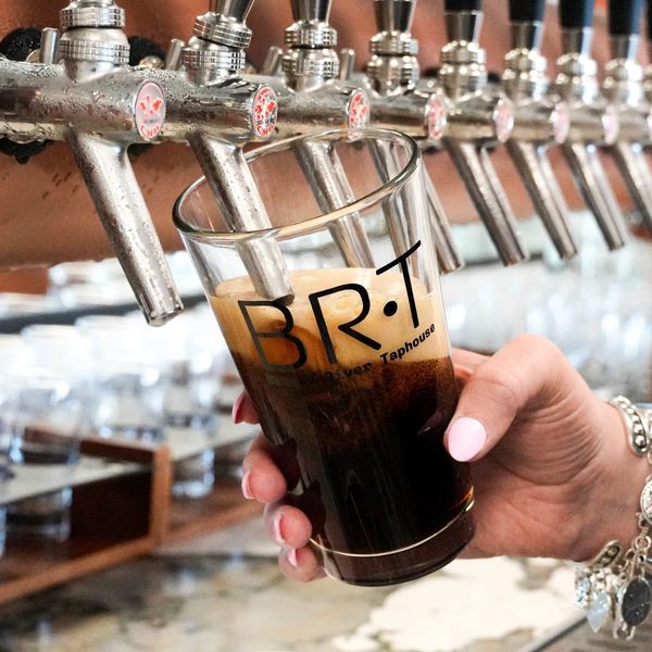 Person filling a dark beer at a brewery tap.