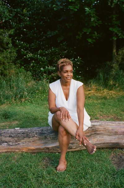 Woman in white dress sitting barefoot on a log outdoors.