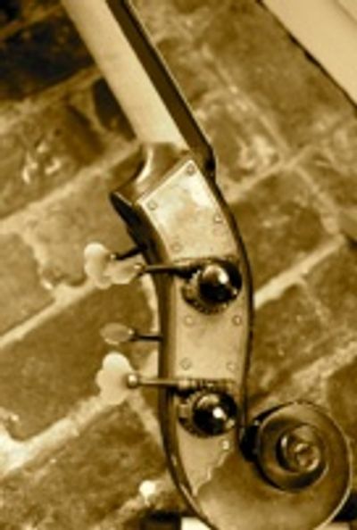 Close-up of a vintage violin scroll and tuning pegs against a brick background.