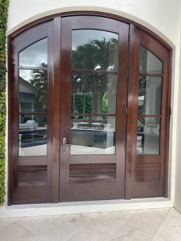 Elegant arched wooden door with glass panels reflecting a patio and pool area.