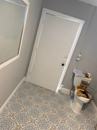 Bathroom with patterned tile floor, white door, and cluttered toilet.