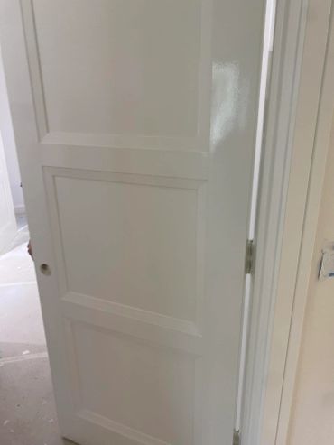 White paneled door partially open in a bright room under renovation.