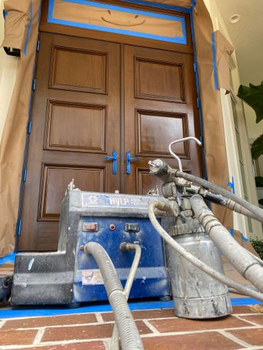 Wooden double doors masked for painting with spray equipment in front.