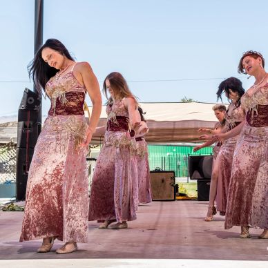 Group of women dancing on stage in coordinated velvet dresses.