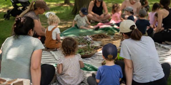 Adults and children sitting on blankets outdoors in a group activity.