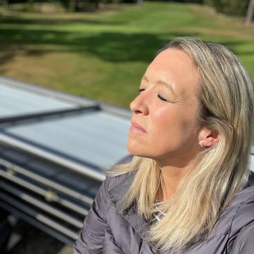 A woman with closed eyes enjoying sunlight outdoors.
