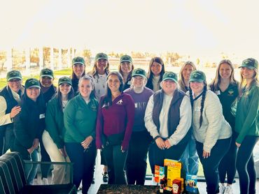 Group of women wearing green hats and casual outdoor clothing, smiling together.
