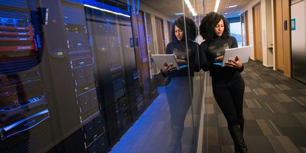 Woman with laptop by server room, symbolizing tech-enabled efficiency and business automation.
