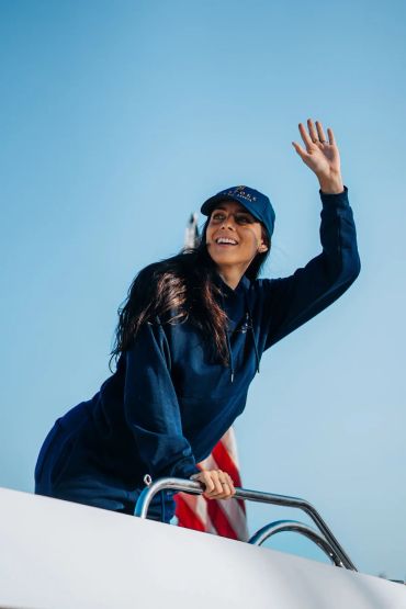Smiling woman waving on a boat under clear blue sky.