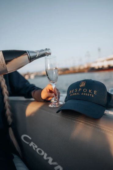 Pouring champagne on a boat with a Bespoke Global Assets hat.