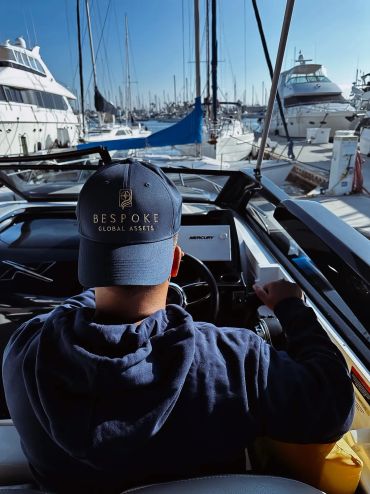 Person steering a boat in a marina with yachts.