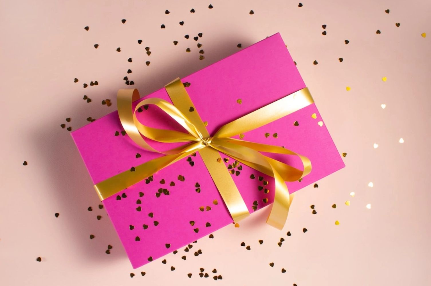 Pink gift box with golden ribbon and confetti.
