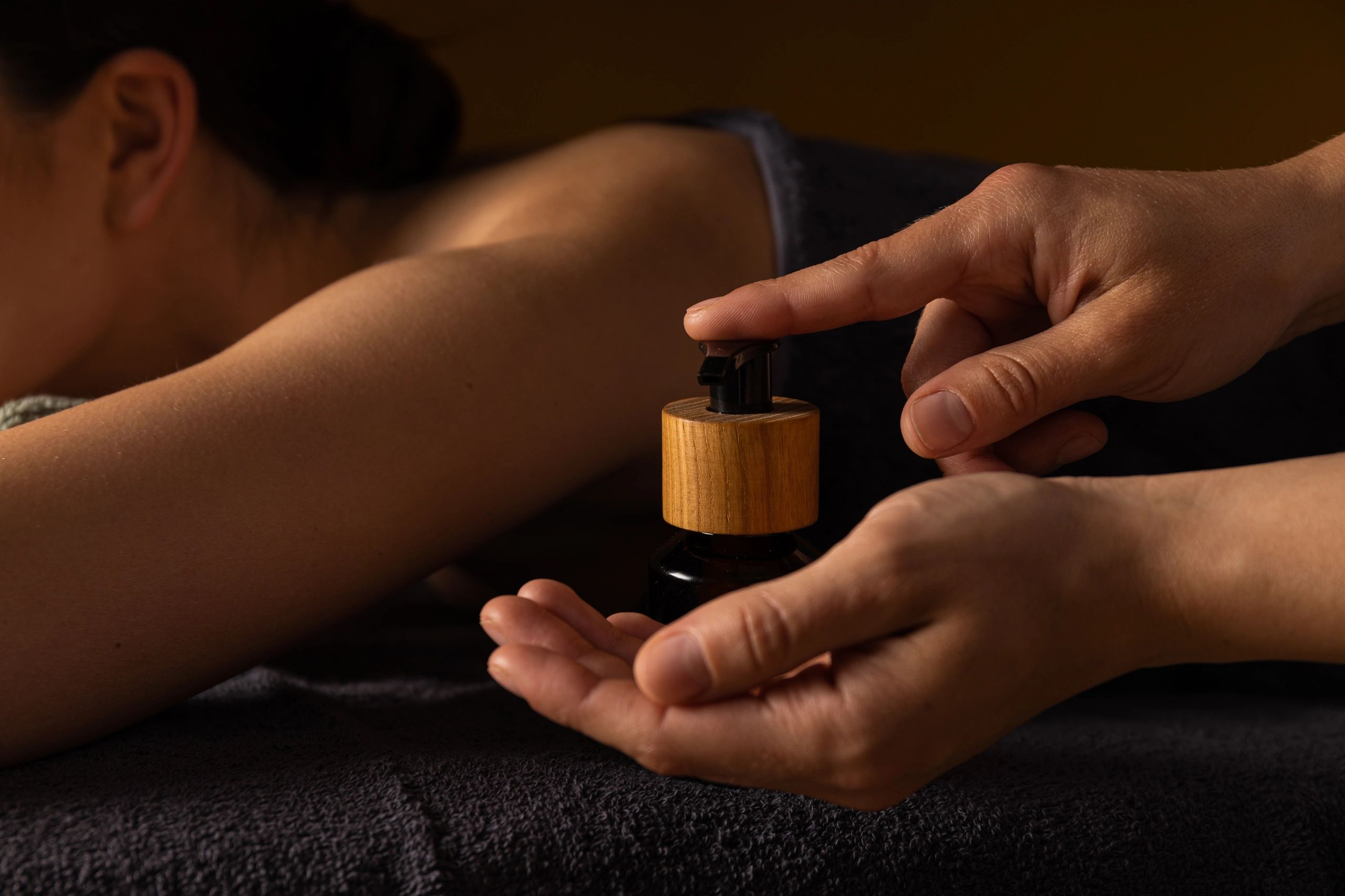Person dispensing oil for a massage on a relaxed arm and shoulder.