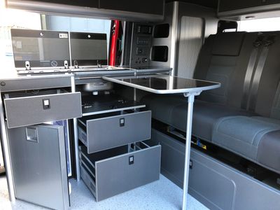 Campervan black interior showing cupboards and draws open with table set up. 