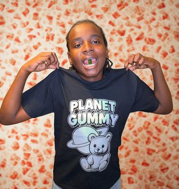 Boy showing off a Planet Gummy t-shirt with a gummy candy in his mouth.