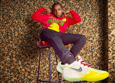 Young person in a red Grinch sweater and bright sneakers sits confidently on a stool.
