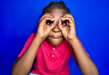 Child making binoculars with hands against a blue background.