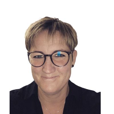 Smiling person with short hair and round glasses against white background.