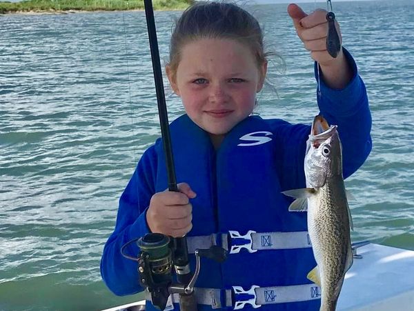 Young girl proudly holds a freshly caught fish on a boat.