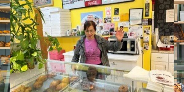 A woman behind a bakery counter waving.