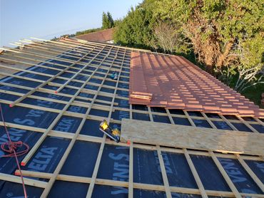Half-finished roof installation with wooden battens and terracotta tiles.