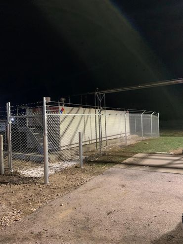 commercial chainlink fence with barb wire and bollard posts that secures a fuel tank at a prison