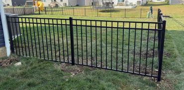 Black metal fence panels installed on a grassy lawn.