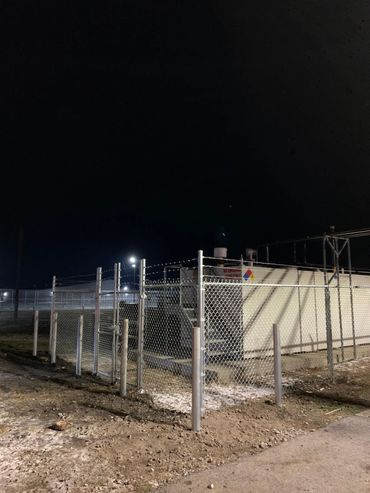 chainlink fence with barb wire and bollard posts enclosing a generator and fuel tank at a prison