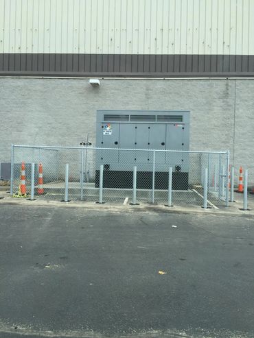 Industrial generator secured behind a chain-link fence with bollard posts