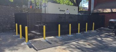 Black fenced enclosure with yellow bollards surrounding a Kohler generator unit.