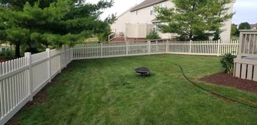 A backyard with a white picket vinyl fence and fire pit.