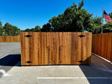 Cedar wood privacy fence with a double gate that serves the purpose of dumpster enclosure.