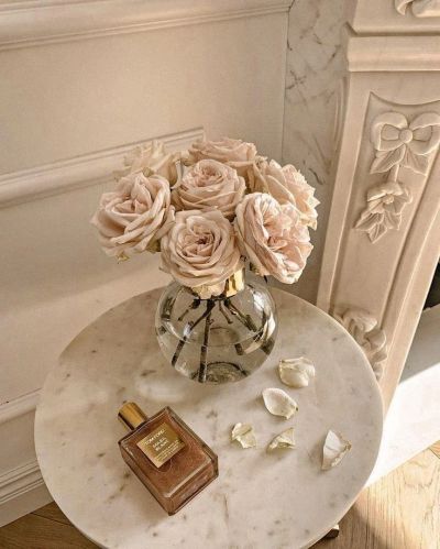 Elegant beige roses in a glass vase with perfume on a marble table.