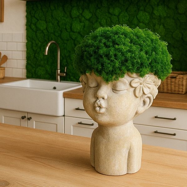 Head planter filled with green preserved moss sits on a light wooden countertop in a bright kitchen.