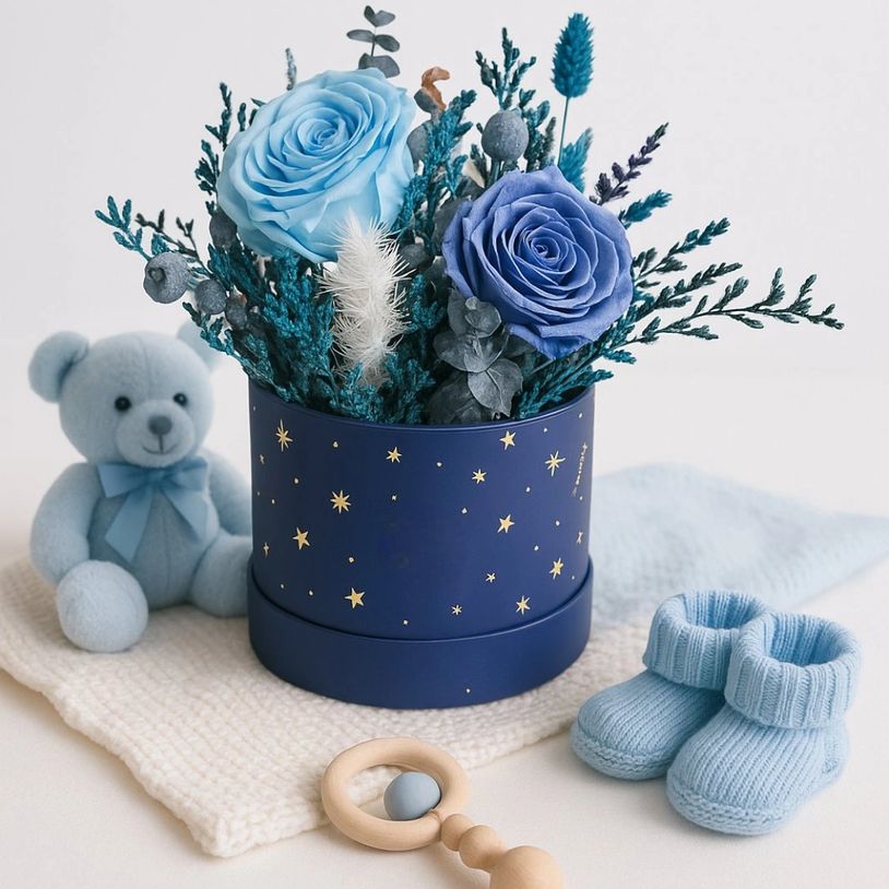 A navy blue round box with preserved light blue roses, along with other preserved foliage